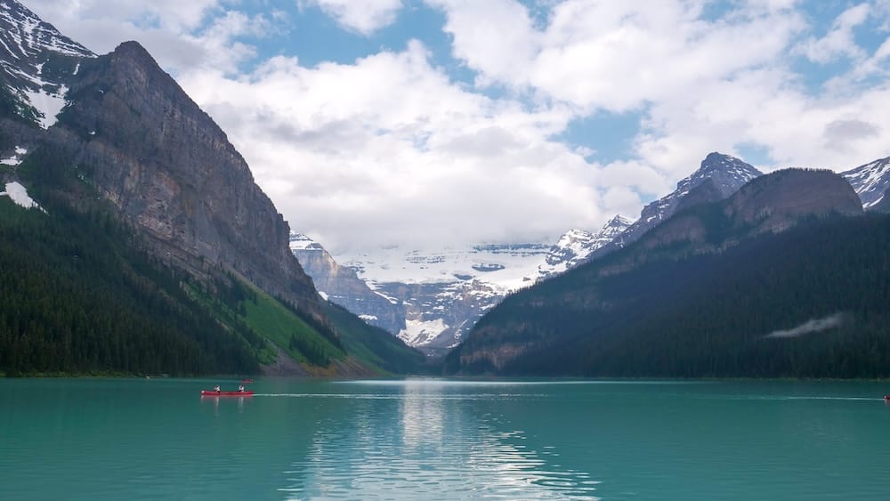 Lake Louise Canoeing With Victoria Glacier in Banff National Park, Alberta, Canada A red canoe crosses the turquoise water of Lake Louise in Banff National Park, Alberta, Canada, with forested mountain walls and Victoria Glacier visible at the far end of the lake.