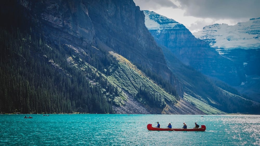 Canoeing on Lake Louise Banff National Park Alberta Canada with turquoise water and mountain scenery A red canoe carrying four people crosses turquoise Lake Louise in Banff National Park, Alberta, Canada, beneath steep forested slopes and snow-covered mountain peaks.