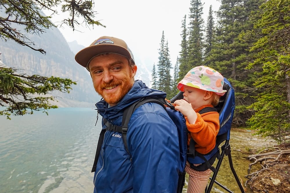 Samuel Jeffery hiking with Aurelia Jeffery at Lake Louise in Banff National Park, Alberta, Canada Samuel Jeffery hikes beside Lake Louise in Banff National Park, Alberta, Canada, carrying Aurelia Jeffery in a child carrier with forest, turquoise water and steep mountain slopes behind them.