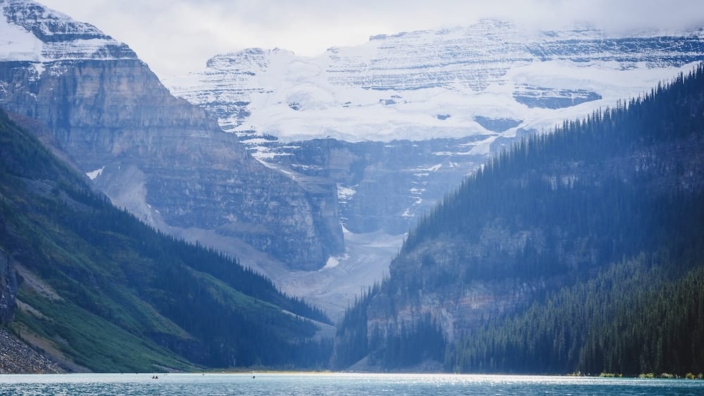 Lake Louise, Banff National Park, Alberta, Canada - glacier-backed mountain scenery and turquoise lakeshore view Lake Louise in Banff National Park, Alberta, Canada, with pale blue water below steep forested slopes and glacier-covered mountains at the far end of the lake, photographed from the shoreline.