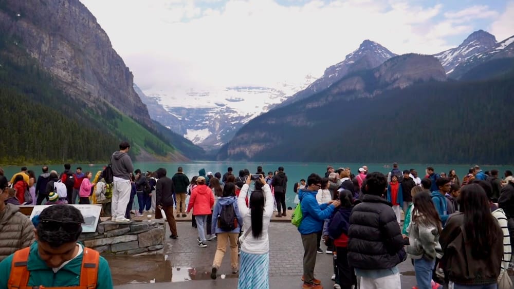 Visitantes fotografiando Lake Louise y el Glaciar Victoria, Parque Nacional Banff, Alberta, Canadá. Decenas de visitantes se alinean en la costa pavimentada de Lake Louise en el Parque Nacional Banff, Alberta, Canadá, fotografiando el lago turquesa y el Glaciar Victoria, con varias personas paradas sobre el muro de contención de piedra para tener un mejor ángulo.