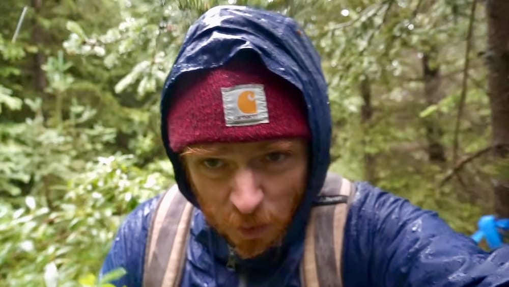 Samuel Jeffery hiking to Lake Matthias in rain during the Banff National Park backcountry horseback trip Samuel Jeffery hikes through wet forest toward Lake Matthias in Banff National Park, Alberta, Canada, wearing a hooded rain jacket and beanie as rain falls during the backcountry rest-day hike.