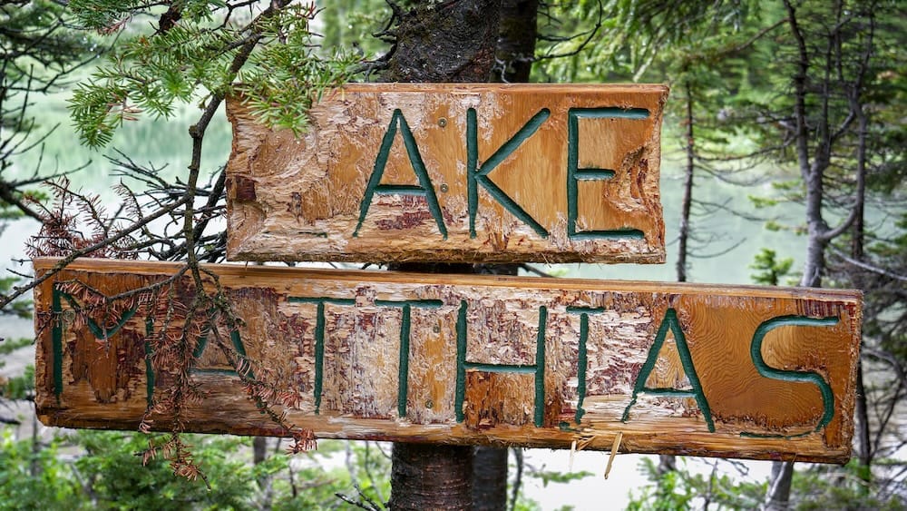 Cartel tallado a mano del lago Matthias, Halfway Lodge, Parque Nacional Banff, Alberta, Canadá Un cartel de madera gastado y tallado a mano que dice "Lake Matthias", con parte de la tabla superior rota, cuelga de un árbol junto al lago cerca de Halfway Lodge en el Parque Nacional Banff, Alberta, Canadá.