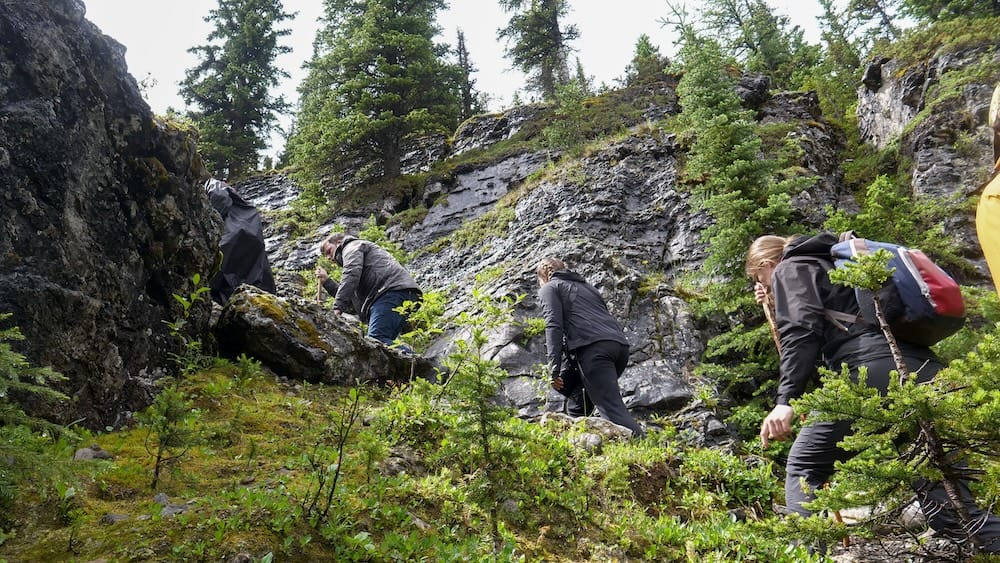 Excursionistas suben por un tramo rocoso, empinado y mojado de la ruta hacia Lake Matthias en el Parque Nacional Banff, Alberta, Canadá, rodeados de coníferas, roca con musgo y vegetación de montaña.