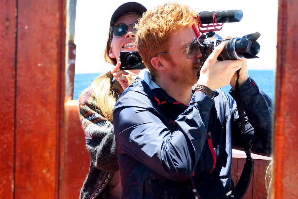 Lake Titicaca, Peru travel filming scene, with Nomadic Samuel recording video on a boat while Audrey Bergner films behind him, capturing real behind-the-scenes creation for the Samuel and Audrey YouTube channel.