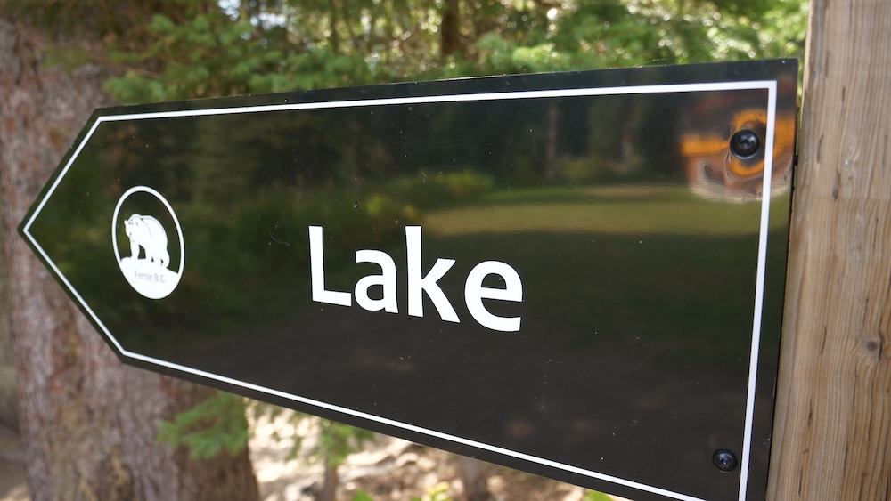 Lake Trail sign at Island Lake Lodge in Fernie, British Columbia, pointing visitors toward the easy lakeside walking trail through forested surroundings, marking the start of one of the lodge’s most popular short hikes for scenic views.
