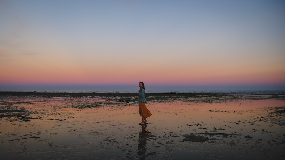 Las Grutas sunset beach in Río Negro Patagonia with Audrey Bergner walking across low tide reflections Las Grutas beach at sunset in Río Negro, Argentina, where Audrey Bergner walks across reflective tidal flats along Patagonia’s Atlantic coast, capturing the calm evening light and wide open shoreline that make this coastal stop a unique northern gateway to Patagonia.