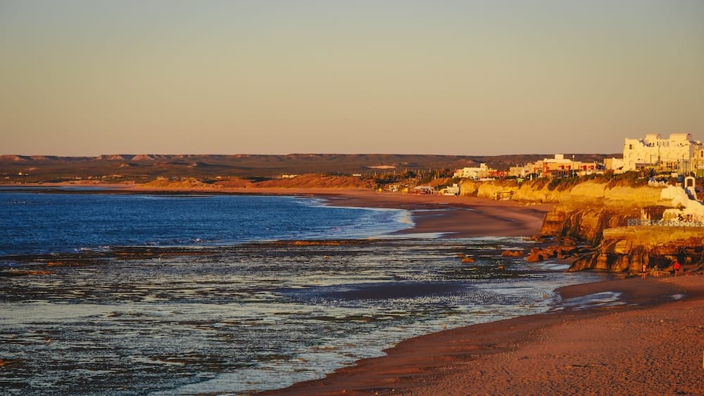Las Grutas Patagonia coastline at golden hour with cliffs tidal flats and Atlantic beach town in Argentina Golden hour over the coastal cliffs and tidal flats of Las Grutas Río Negro Argentina with warm sunlight illuminating the Atlantic shoreline and beach town along the Patagonian coast.