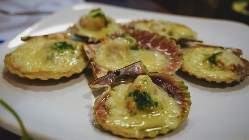 Gratinéed Patagonian scallops served in their shells in Las Grutas, Río Negro, Argentina, highlighting vieiras from the warm-water Gulf of San Matías known for their briny flavor and role in coastal mariscos dishes.