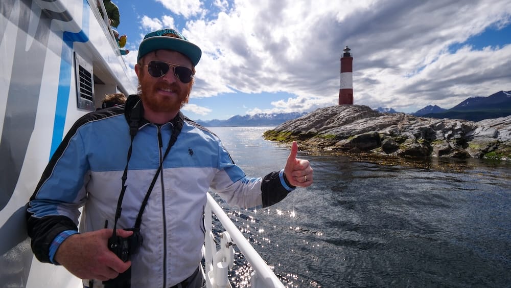 Les Eclaireurs Lighthouse boat tour on the Beagle Channel near Ushuaia, Tierra del Fuego, Patagonia, Argentina Samuel Jeffery gives a thumbs up aboard a Beagle Channel boat tour, with the red-and-white Les Eclaireurs Lighthouse and the mountains of Tierra del Fuego rising behind him near Ushuaia, Patagonia, Argentina.