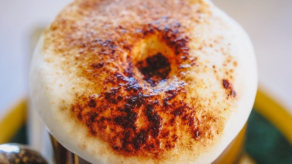 Close-up of a frothy cappuccino dusted with cinnamon during afternoon tea at Llao Llao Hotel in Bariloche, Río Negro, Patagonia, Argentina, with caramelized foam filling the frame.