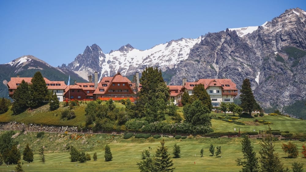 Llao Llao Hotel architecture beneath snowy peaks in Bariloche, Patagonia, Argentina Llao Llao Hotel’s red-roofed timber architecture sits among landscaped lawns in Bariloche, Río Negro, Patagonia, Argentina, with steep rocky mountains and lingering snow rising directly behind the resort.