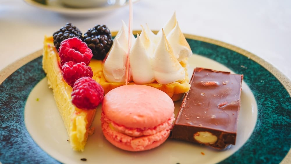 Afternoon tea desserts at Llao Llao Hotel in Bariloche, Río Negro, Argentina, including a pink macaron, meringue-topped tart, chocolate confection and fresh raspberries and blackberries.