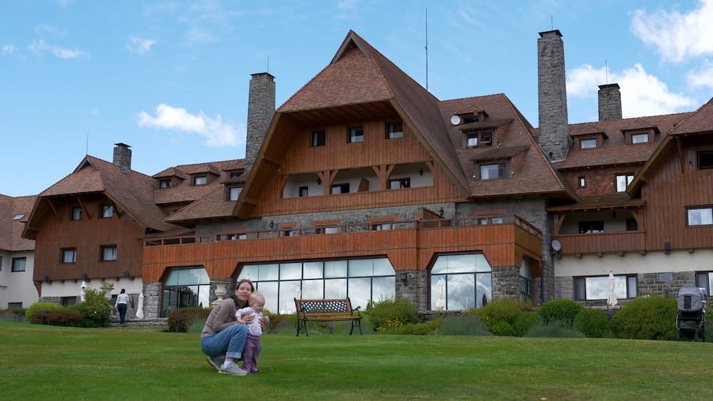 Llao Llao Hotel alpine architecture in Bariloche, Río Negro, Argentina, with Audrey Bergner and Aurelia Jeffery Audrey Bergner crouches beside Aurelia Jeffery on the lawn below Llao Llao Hotel, showing its timber balconies, steep alpine roofs and stone chimneys in Bariloche, Río Negro, Patagonia, Argentina.