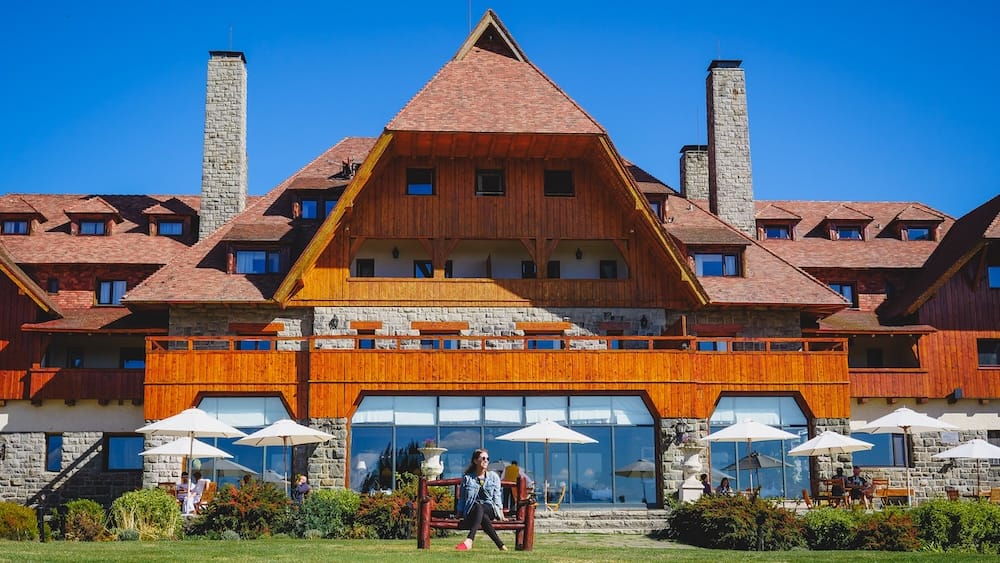 Audrey Bergner rests on a wooden bench in the landscaped gardens before the timber-and-stone facade of Llao Llao Hotel in Bariloche, Río Negro, Patagonia, Argentina.