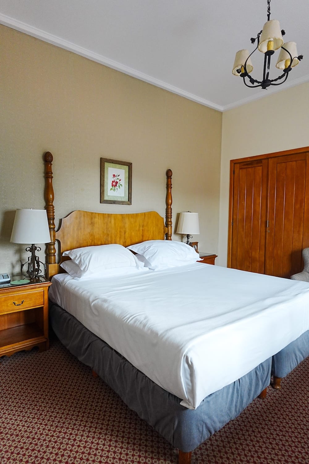 Standard-style guest room at Llao Llao Hotel in Bariloche, Río Negro, Argentina, featuring a classic wooden bedframe, bedside tables, floral wall art, carpeted floor and traditional alpine-style decor.