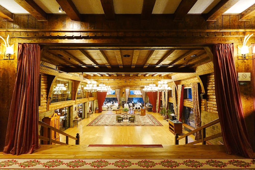 Grand interior hall at Llao Llao Hotel in Bariloche, Río Negro, Argentina, with timber beams, chandeliers, patterned rugs, sweeping stairs and an elegant dining area visible beyond.
