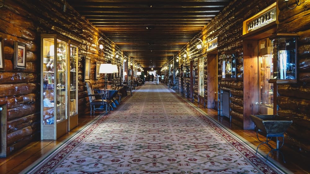 Long interior corridor at Llao Llao Hotel in Bariloche, Río Negro, Argentina, lined with dark timber walls, patterned carpet, display cabinets, boutique entrances and warm lodge-style lighting.