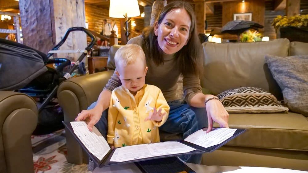 Audrey Bergner and Aurelia Jeffery Reviewing a Menu at Llao Llao Hotel, Bariloche, Patagonia, Argentina Audrey Bergner and Aurelia Jeffery review a restaurant menu together inside Llao Llao Hotel in Bariloche, Río Negro, Patagonia, Argentina, seated beside a stroller in the resort’s warm wood-lined lounge interior.