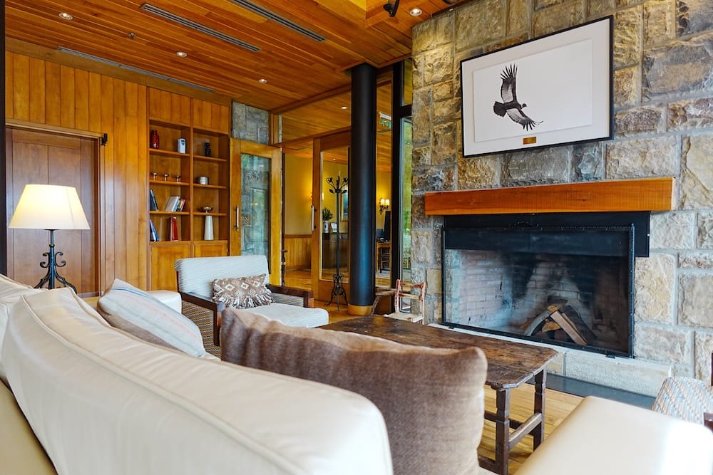 Stone fireplace and timber lounge inside Llao Llao Hotel in Bariloche, Río Negro, Argentina, with upholstered seating, built-in shelves, warm wood ceilings and framed condor artwork above the hearth.