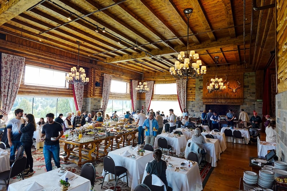 Breakfast buffet service fills the grand timber dining hall at Llao Llao Hotel in Bariloche, Río Negro, Patagonia, Argentina, with guests seated beneath chandeliers and exposed wooden beams.