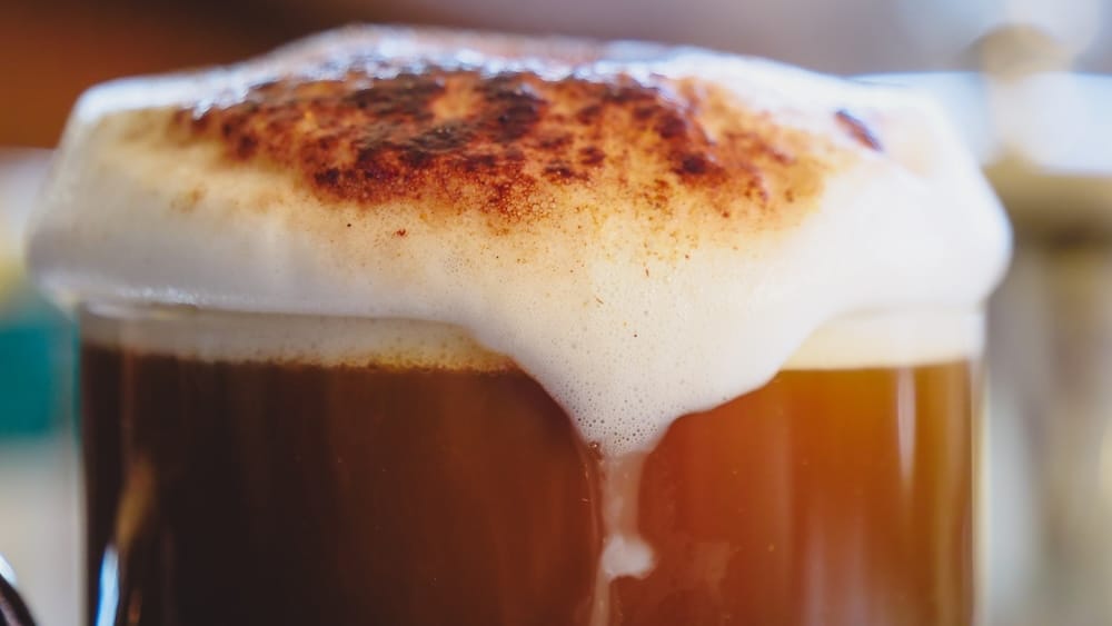 Cappuccino with cinnamon-dusted foam, Llao Llao Hotel afternoon tea, Winter Garden, Bariloche, Río Negro, Argentine Patagonia Close-up of a cinnamon-dusted cappuccino with thick foam overflowing the glass, part of the afternoon tea service at Llao Llao Hotel's Winter Garden near Bariloche, Río Negro, in Argentine Patagonia.