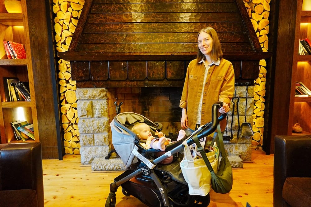 Audrey Bergner stands beside Aurelia Jeffery in a stroller before a large stone-and-wood fireplace inside Llao Llao Hotel in Bariloche, Río Negro, Patagonia, Argentina.