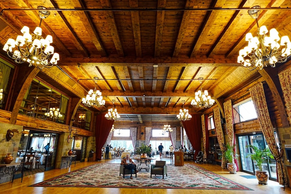 The wood-beamed central hallway of the Llao Llao Hotel, with tall stone arches, ornate chandeliers, a patterned rug, and guests seated in the lounge area, San Carlos de Bariloche, Rio Negro, Argentine Patagonia.