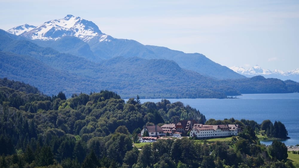Llao Llao Hotel above Nahuel Huapi Lake with Andean mountain backdrop in Bariloche, Patagonia, Argentina Llao Llao Hotel sits above Nahuel Huapi Lake in Bariloche, Río Negro, Patagonia, Argentina, surrounded by dense forest, with blue water and layered Andean peaks rising behind the resort under clear daylight.