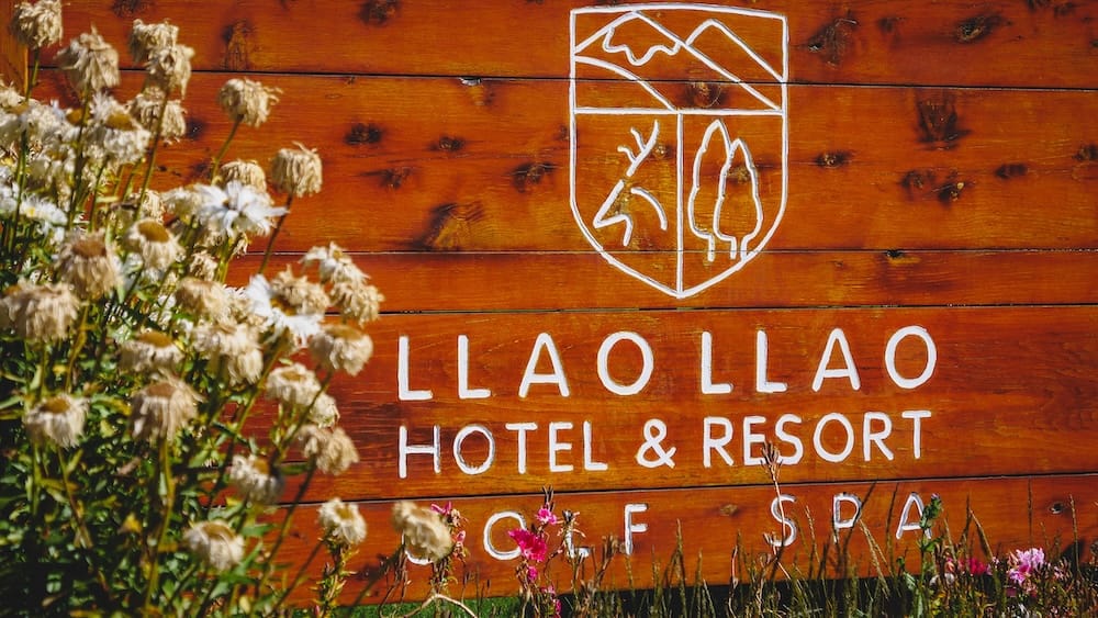 Llao Llao Hotel & Resort Golf Spa wooden crest sign, Bariloche, Río Negro, Argentine Patagonia Wooden entrance sign painted with the Llao Llao Hotel & Resort crest, reading "Llao Llao Hotel & Resort Golf Spa," framed by wildflowers, near Bariloche, Río Negro, in Argentine Patagonia.