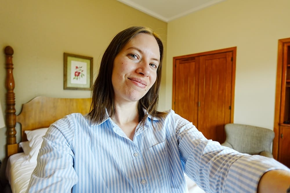 Audrey Bergner takes a selfie inside a heritage-style Llao Llao Hotel room in Bariloche, Río Negro, Patagonia, Argentina, with a carved wooden bed, armchair, wardrobe and warm timber furnishings behind her.