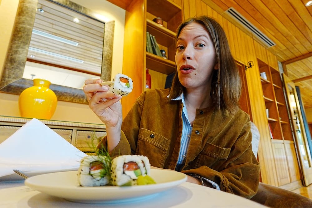 Audrey Bergner holds a piece of salmon, avocado and cream cheese sushi while dining inside Llao Llao Hotel in Bariloche, Río Negro, Patagonia, Argentina, with a plate of rolls in front of her.