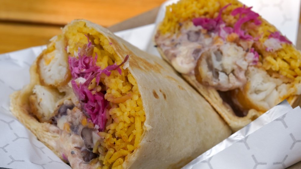 Fishy Boy Burrito Macro Close-Up at Luchadora Burrito Co. in Fernie, BC Fernie, British Columbia macro food photo of the Fishy Boy burrito from Luchadora Burrito Co., cut in half to show crispy battered cod, fluffy spicy yellow rice, black beans, pickled purple cabbage, melted cheese, and creamy habanero lime aioli inside a warm tortilla.