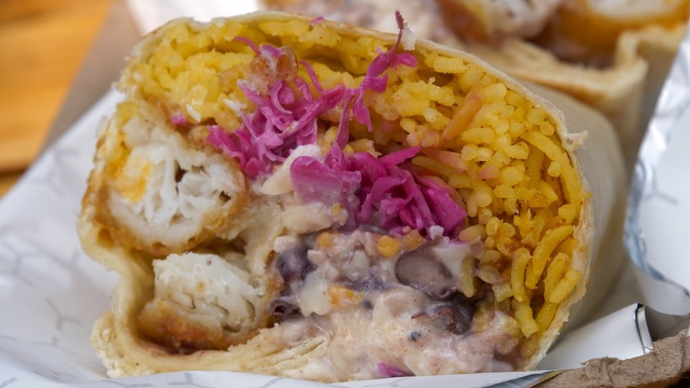 Fishy Boy Burrito Macro Detail at Luchadora Burrito Co. in Fernie, BC Fernie, British Columbia macro food shot of the Fishy Boy burrito from Luchadora Burrito Co., sliced open to reveal crispy battered cod, fluffy spicy yellow rice, black beans, pickled purple cabbage, melted cheese, and tangy habanero lime aioli inside a soft tortilla.