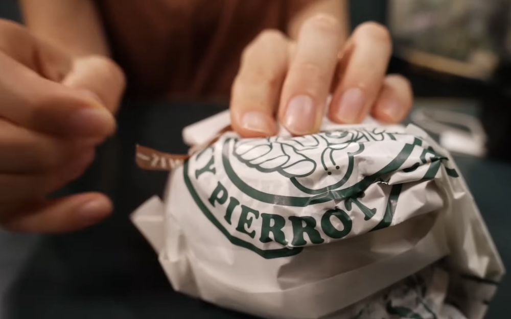 Audrey Bergner desenvolviendo una hamburguesa en Lucky Pierrot cerca de Goryokaku, Hakodate, Hokkaido, Japón Manos de Audrey Bergner desenvolviendo una hamburguesa en papel verde y blanco de Lucky Pierrot con el logo del payaso y el nombre impreso, en una mesa en Hakodate, Hokkaido, Japón.