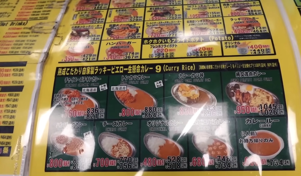 Cartel del menú de Lucky Pierrot con hamburguesas, papas fritas y curry cerca de Goryokaku, Hakodate, Hokkaido, Japón Cartel de menú amarillo en un restaurante Lucky Pierrot en Hakodate, Hokkaido, Japón, con hamburguesas, papas fritas y una sección verde de nueve platos de arroz con curry con fotos y precios en japonés e inglés.