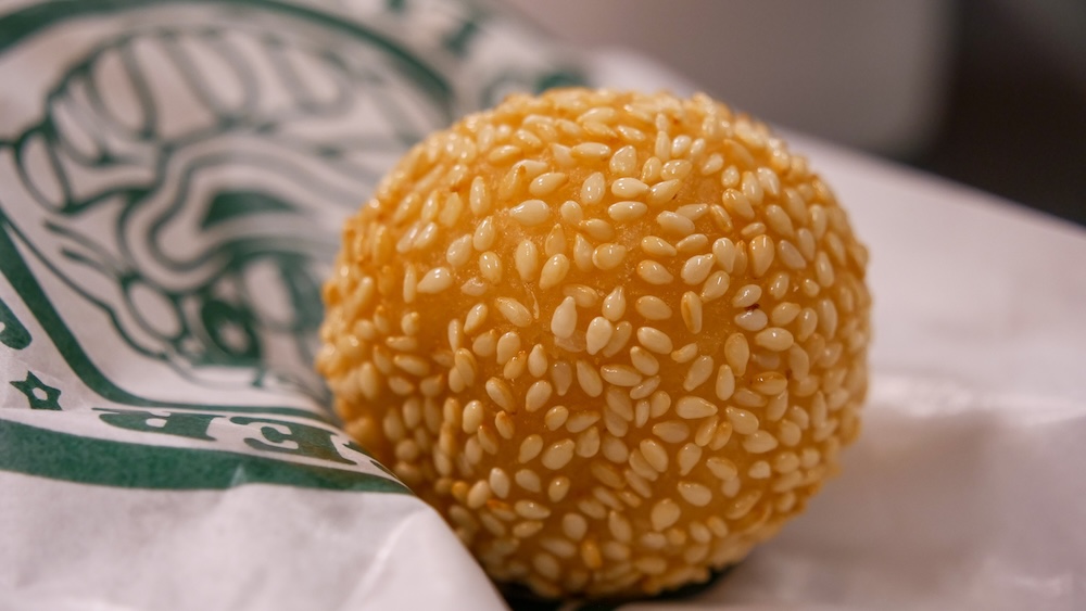 Primer plano de bolita de sésamo de postre en Lucky Pierrot cerca de Goryokaku, Hakodate, Hokkaido, Japón Primer plano de una bolita de sésamo frita y dorada cubierta de semillas de sésamo blancas sobre papel impreso verde y blanco en un restaurante Lucky Pierrot en Hakodate, Hokkaido, Japón.