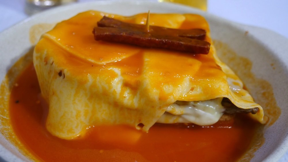 Macro details eating a Francesinha Portuguese Sandwich layered with ham, sausage, beef, melted cheese, and crowned with a rich tomato-beer sauce in Porto, Portugal