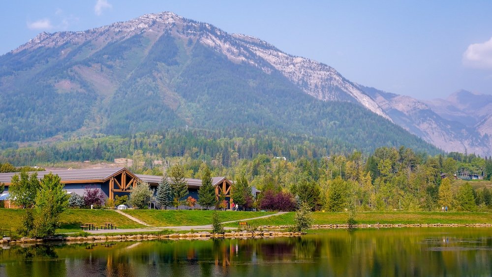 Maiden Lake Fernie BC scenic reflections behind commercial buildings in town Maiden Lake in Fernie, British Columbia showing calm water reflecting Mount Trinity and surrounding forest, with nearby commercial buildings subtly visible behind the shoreline, highlighting how this scenic lake sits right in the heart of town.