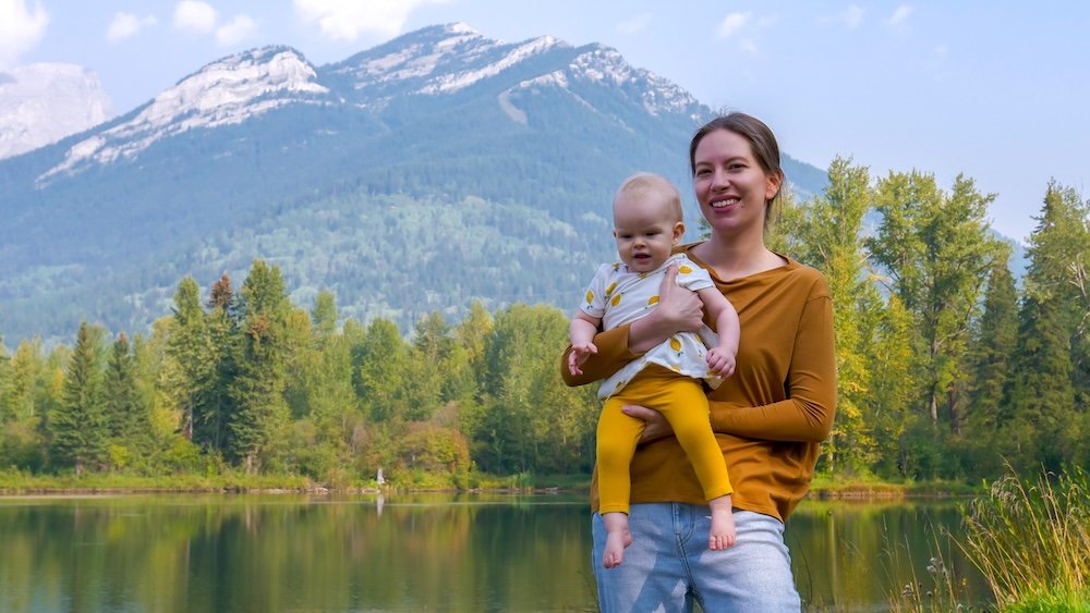 Maiden Lake in Fernie, British Columbia with Audrey Bergner holding baby Aurelia beside the calm shoreline, showcasing Fernie’s family-friendly nature, scenic mountain backdrops, and peaceful outdoor spaces that fit perfectly into a relaxed two-day Fernie itinerary.