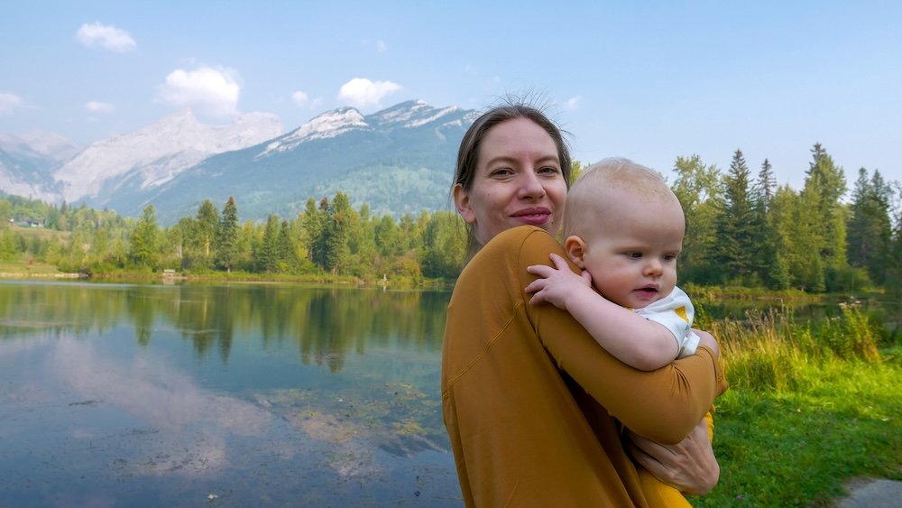 Maiden Lake Fernie BC family photo with Audrey Bergner and baby Aurelia Maiden Lake in Fernie, British Columbia with calm water and mountain reflections as Audrey Bergner holds baby Aurelia during a relaxed lakeside moment, capturing a sweet family memory at one of Fernie’s most scenic in-town spots.