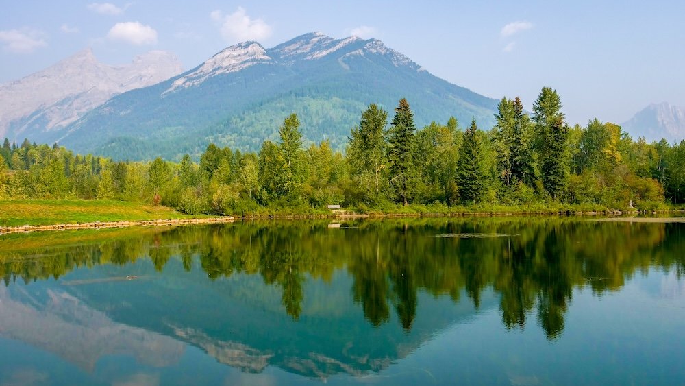 Maiden Lake Fernie BC reflection photography with Mount Trinity and calm water Maiden Lake in Fernie, British Columbia with glassy water reflecting Mount Trinity and dense forest, creating a classic mirror-like scene ideal for photographers looking to capture calm conditions and the natural beauty of the Canadian Rockies.
