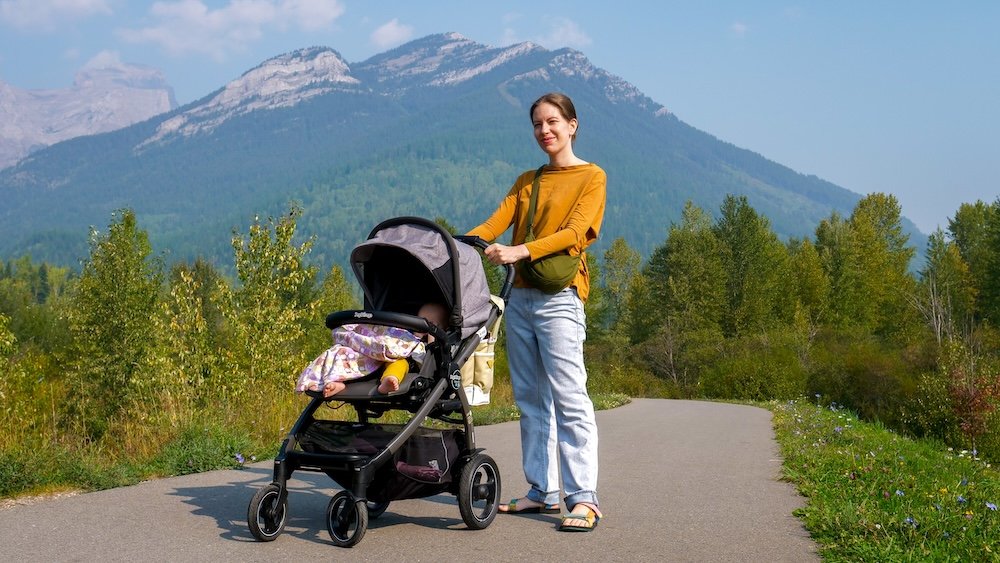 Maiden Lake Fernie BC stroller-friendly path with Audrey Bergner and baby Aurelia Maiden Lake in Fernie, British Columbia with Mount Trinity in the background as Audrey Bergner walks the paved lakeside path pushing baby Aurelia in a stroller, highlighting one of the town’s easiest and most family-friendly scenic strolls.