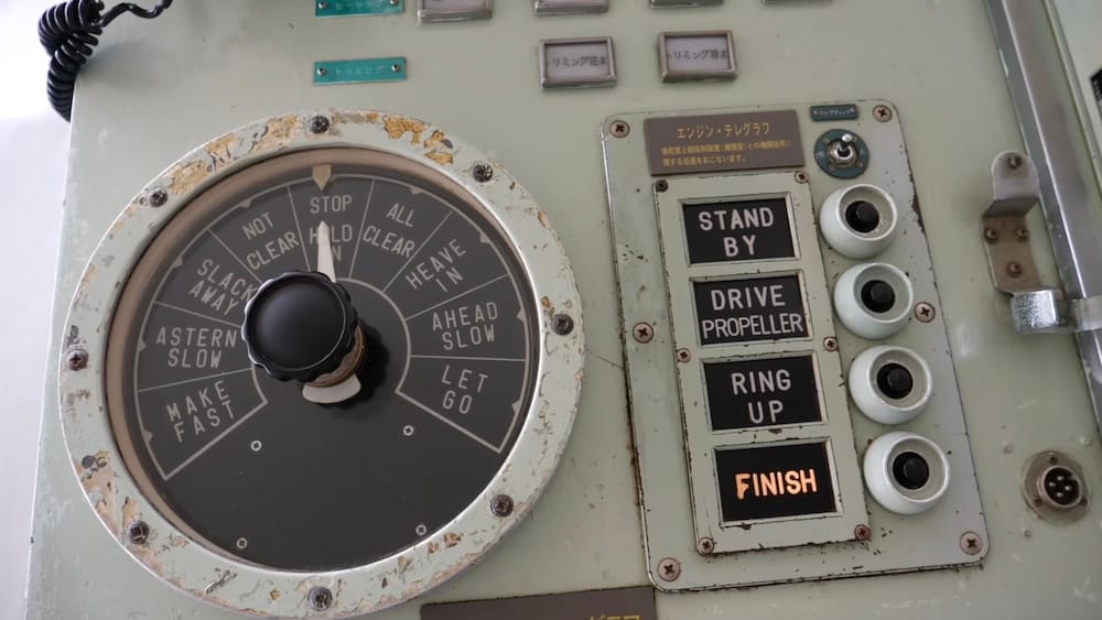 Close-up of vintage ship controls aboard the preserved Mashu-maru in Hakodate, Hokkaido, Japan, showing an engine telegraph dial, propeller controls and worn maritime equipment.