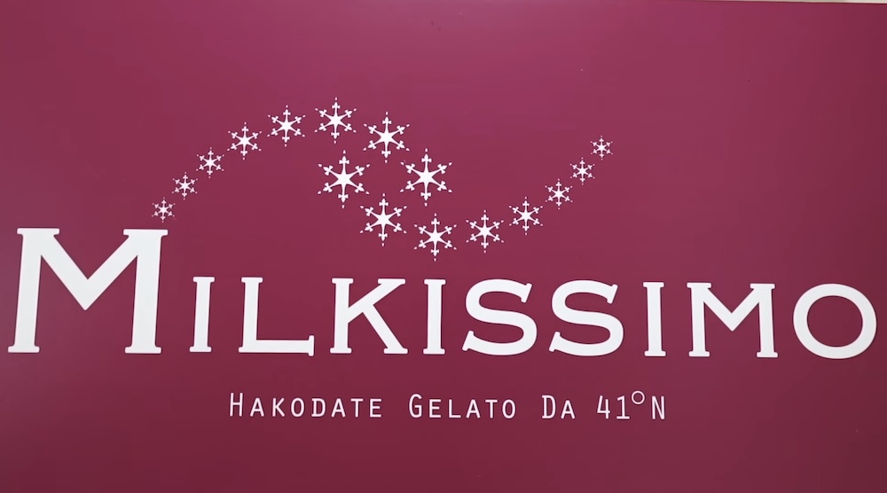 Cartel bordó de Milkissimo con letras blancas, un remolino de copos de nieve y el lema Hakodate Gelato da 41°N, en la heladería dentro de la Torre Goryokaku en Hakodate, Hokkaido, Japón.