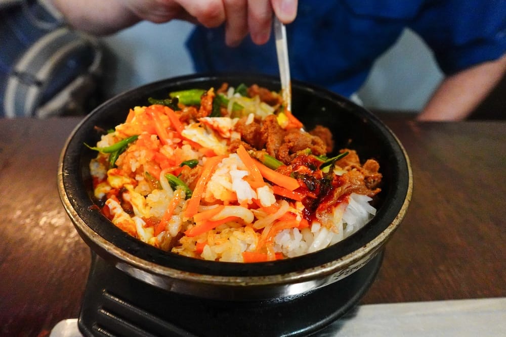 Close-up of stone-pot bibimbap at Moon Korean Cuisine in Calgary, Alberta, Canada, with rice, vegetables, egg and meat being mixed together in the hot bowl during the city’s international-food exploration.