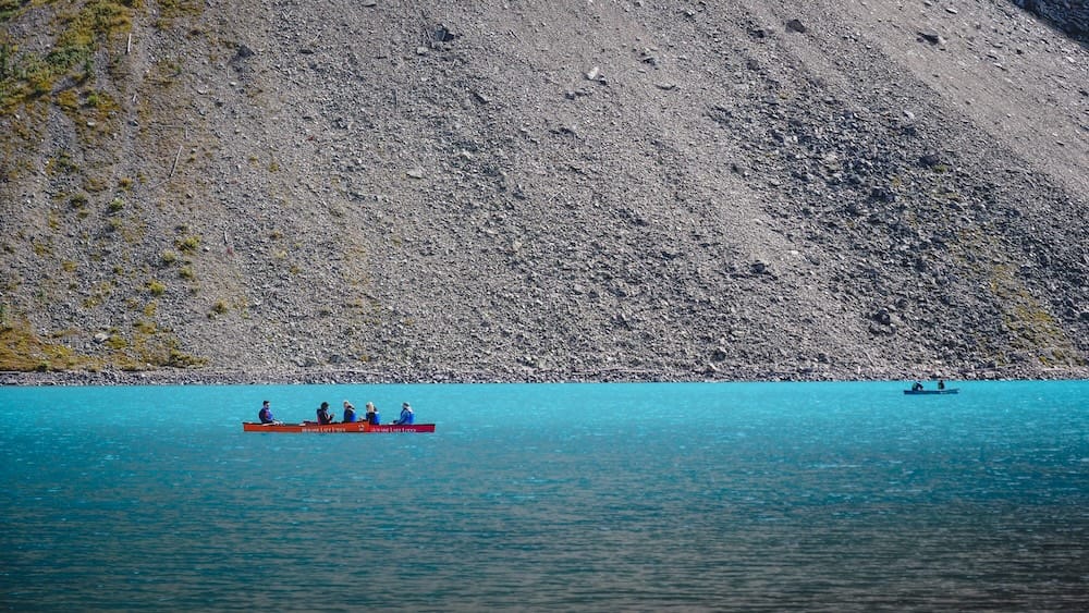 Canoeing on Moraine Lake in Banff National Park, Alberta, Canada, beneath a steep Rocky Mountain slope Two canoes cross the turquoise water of Moraine Lake in Banff National Park, Alberta, Canada, with paddlers in the foreground and a steep gray rocky mountain slope rising behind them.