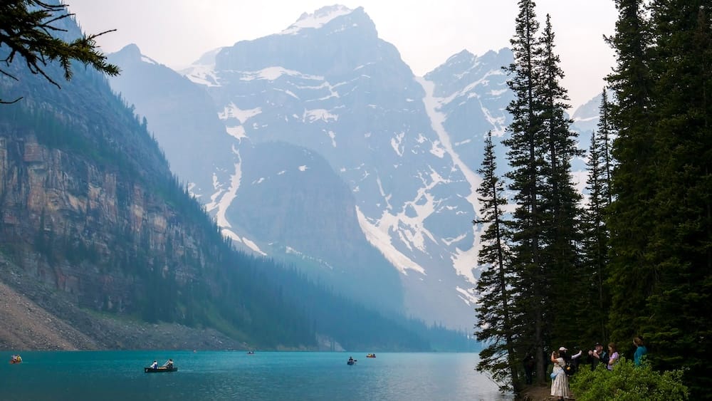 Paseo en canoa por Moraine Lake, en el Parque Nacional Banff, Alberta, Canadá, bajo los picos de las Montañas Rocosas Canoas cruzan las aguas turquesas de Moraine Lake en el Parque Nacional Banff, Alberta, Canadá, con picos de las Montañas Rocosas, bosque de coníferas y visitantes junto a la orilla.