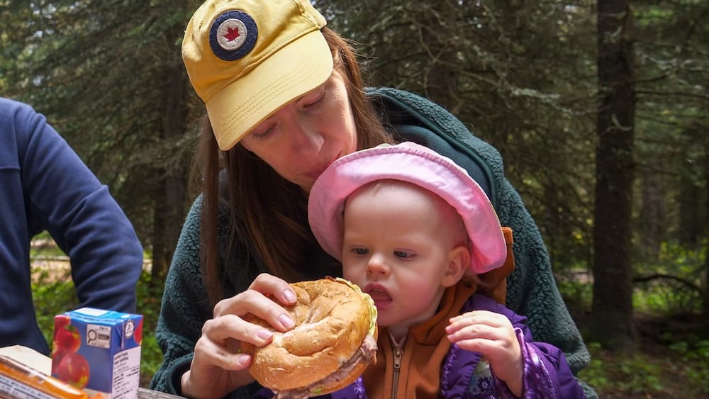 Audrey Bergner and Aurelia Jeffery at a Moraine Lake Picnic in Banff National Park, Alberta, Canada Audrey Bergner shares a roast beef sandwich with Aurelia Jeffery during a family picnic at Moraine Lake in Banff National Park, Alberta, Canada, with evergreen forest surrounding the picnic area.