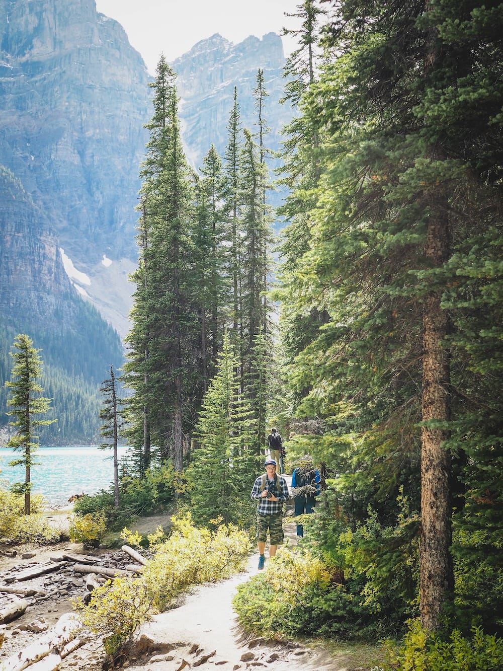 Samuel Jeffery Hiking Beside Moraine Lake in Banff National Park, Alberta, Canada Samuel Jeffery hiking on a forested path beside the turquoise water of Moraine Lake in Banff National Park, Alberta, Canada, with conifer trees and steep Rocky Mountain peaks behind him.
